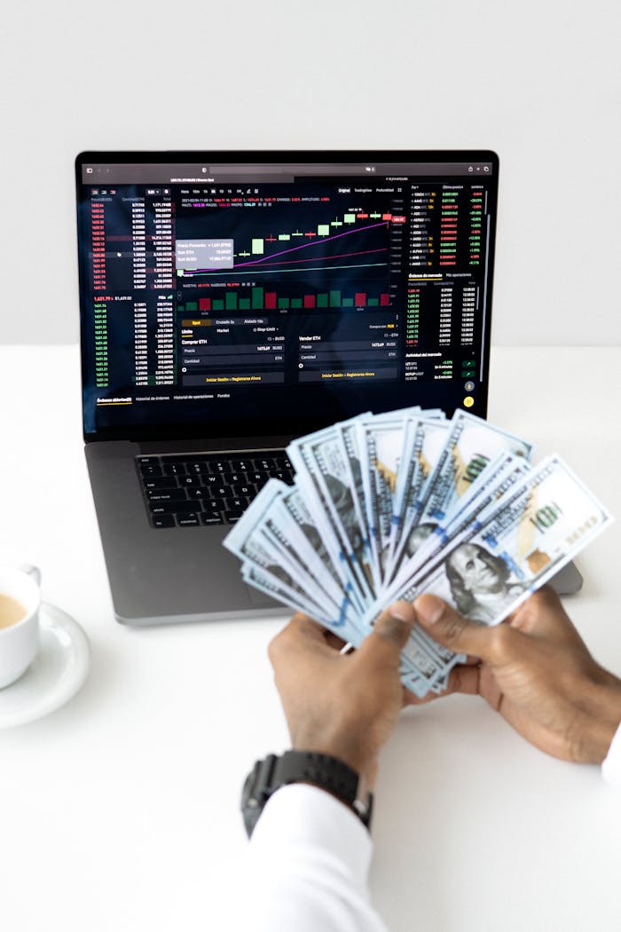 journey Hands holding cash in front of a laptop displaying stock market data, symbolizing financial growth and investment.